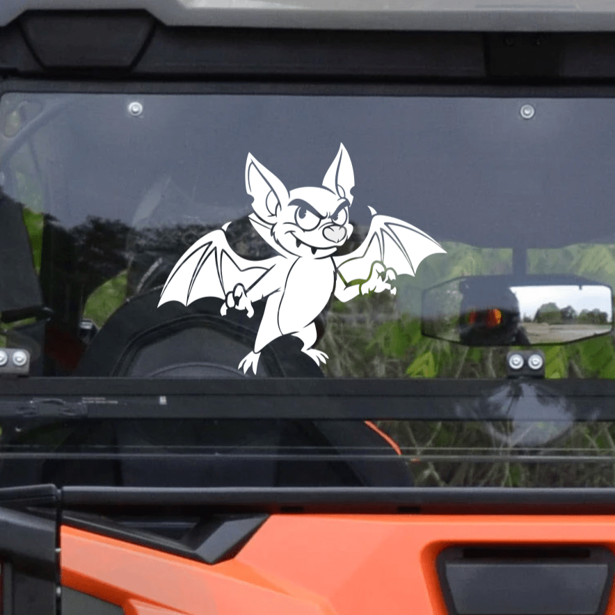 Orange and black UTV with a bat decal on the windshield, surrounded by greenery.