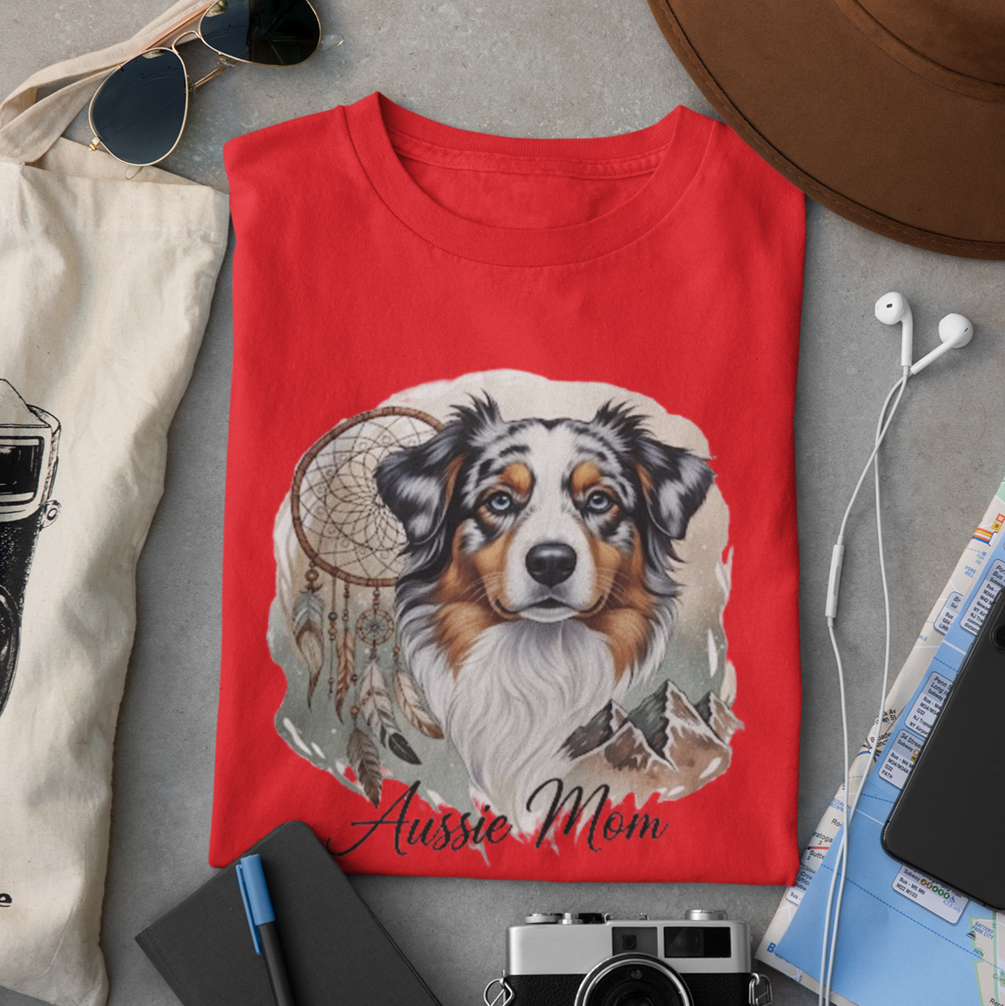 Red t-shirt with a dog illustration and 'Aussie Mom' text, surrounded by casual items on a gray surface.