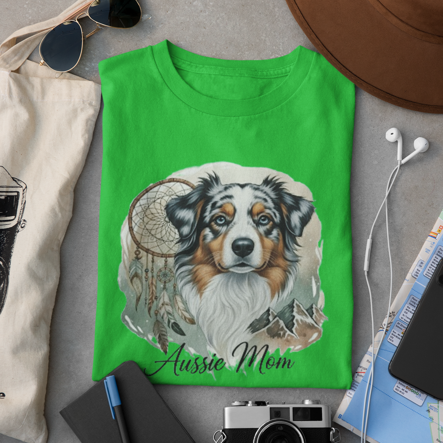 Green t-shirt with a dog illustration and 'Aussie Mom' text, surrounded by casual items on a gray surface.
