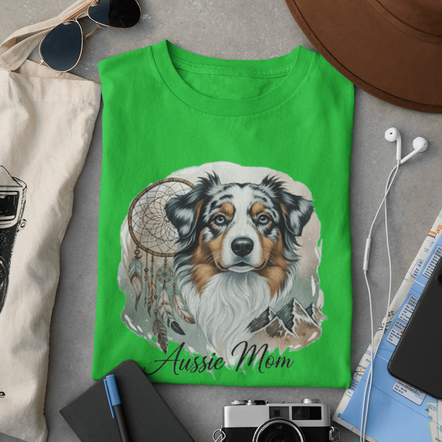Green t-shirt with a dog illustration and 'Aussie Mom' text, surrounded by casual items on a gray surface.