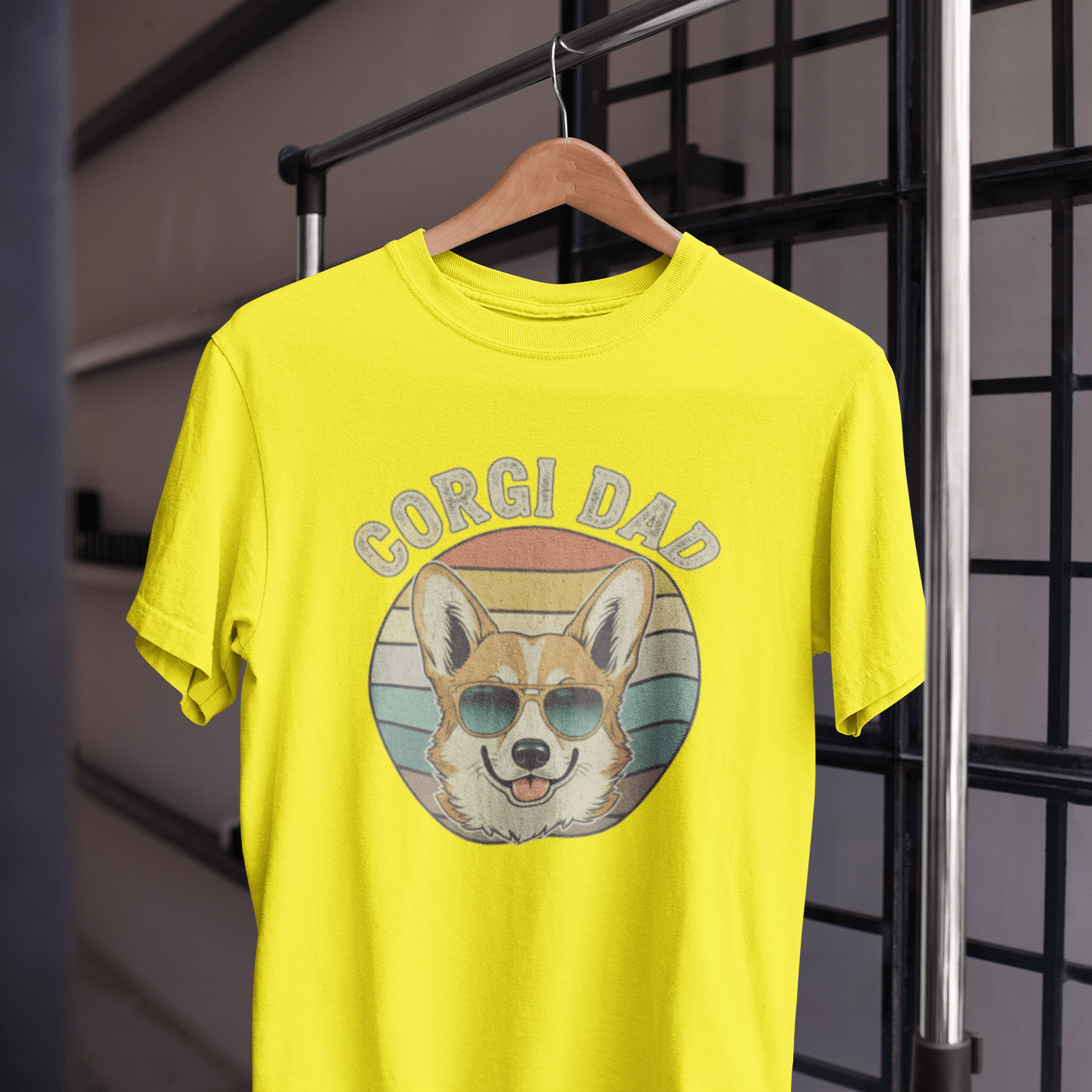 Yellow t-shirt with 'Corgi Dad' graphic on a hanger against a grid background