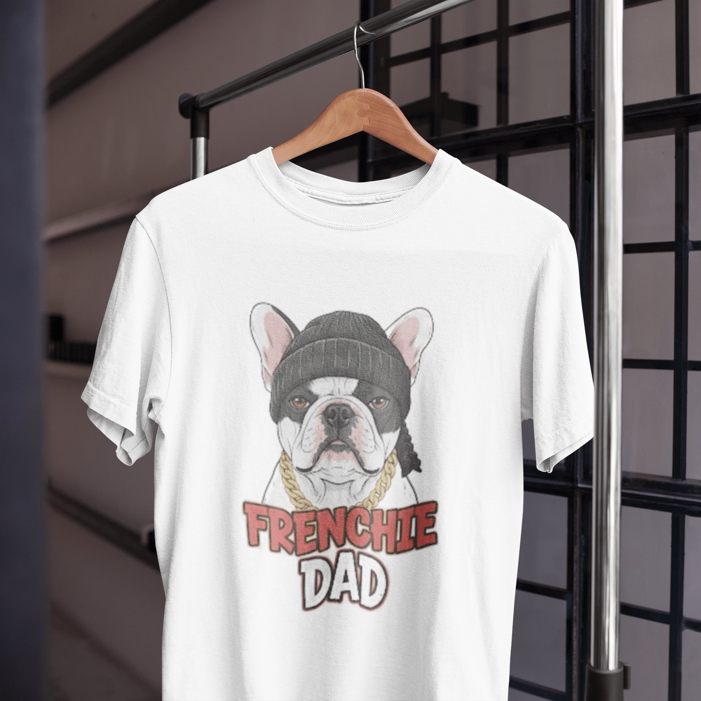 White t-shirt with a graphic of a bulldog wearing a beanie and 'FRENCHIE DAD' text on a hanger.