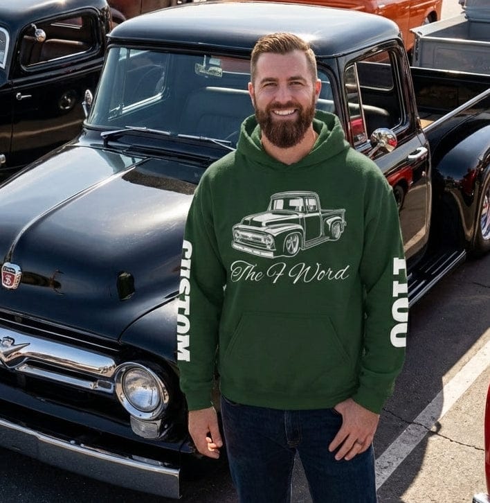 Man in a green hoodie standing in front of vintage trucks at a car show.