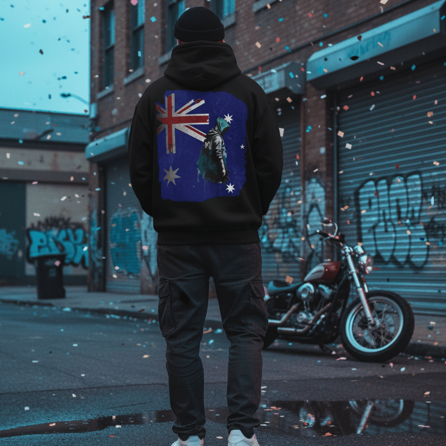 male model wearing a black, oversized hoodie with a distressed Australian Flag graphic on the back, styled with a beanie and sunglasses in an edgy, dark, street-style shoot.