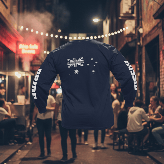 A navy blue long-sleeved t-shirt is shown from the back against a white background. Centered on the upper back is a large, distressed, monochrome print of the Australian flag in white and grey. The left sleeve features the word "PRIDE" in bold, white, vertical block lettering, while the right sleeve features the word "AUSSIE" in the same style. The shirt has ribbed cuffs and a crew neck.