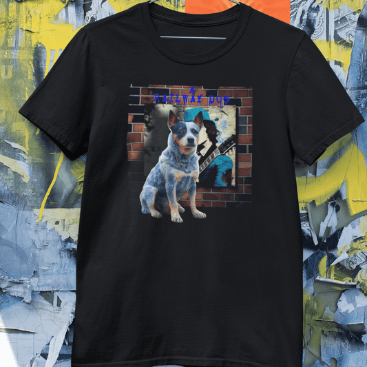 Black graphic t-shirt hanging against a distressed poster wall, featuring an Australian Cattle Dog Blue Heeler sitting in front of a brick wall mural with an electric guitar player and "A Railway Dog" text.