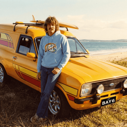 Man leaning against a yellow van with a surfboard on a beach