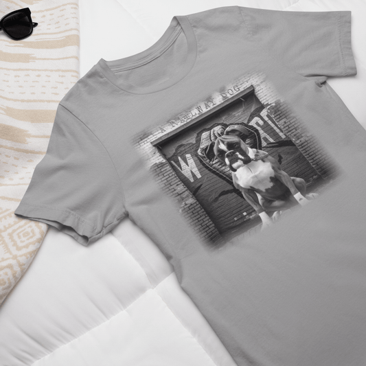 Flat-lay display of a heather grey graphic t-shirt featuring a Boxer dog in hand wraps in front of an urban brick gym doorway with "A Railway Dog" stencil text, styled on a white bed with sunglasses.
