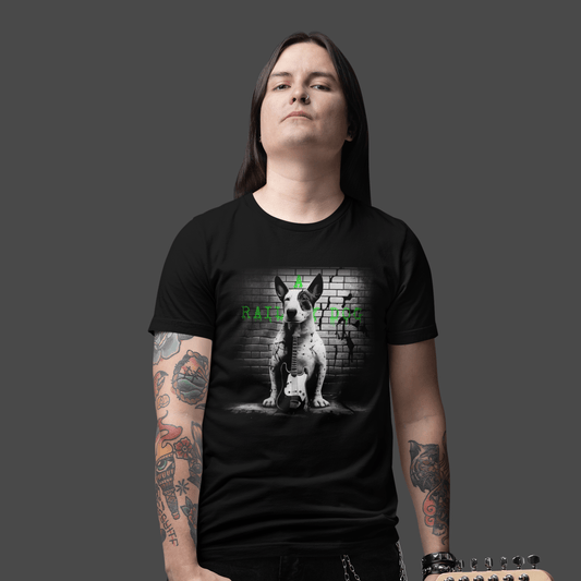 Long-haired man with arm tattoos wearing a black graphic t-shirt featuring a black and white Bull Terrier sitting with a bass guitar in front of a brick wall with green "A Railway Dog" text.