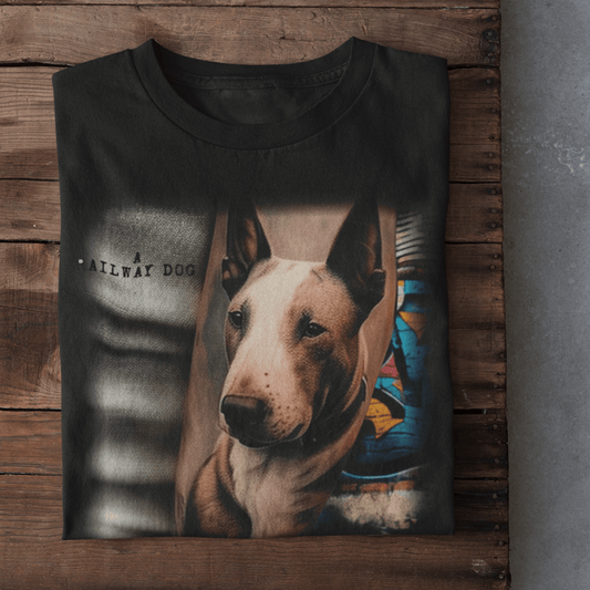 Flat-lay mockup of a neatly folded black graphic t-shirt displayed on a rustic wooden plank surface, featuring an English Bull Terrier portrait set against an urban street art background with stencil text reading "A Railway Dog".