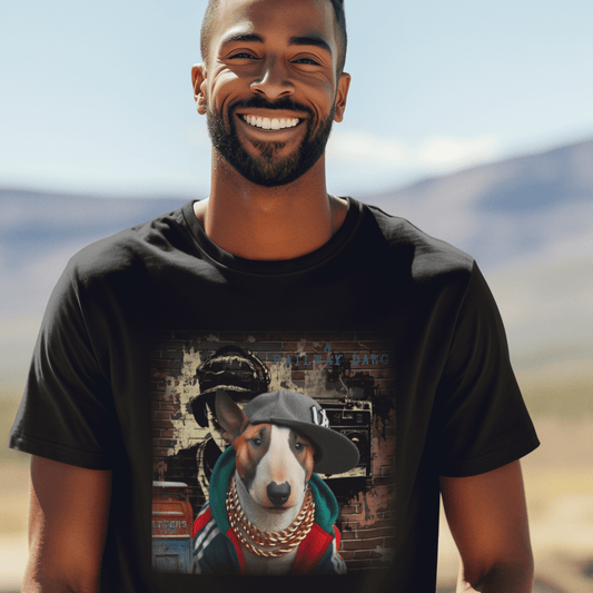 Smiling bearded man outdoors wearing a black graphic t-shirt featuring a Bull Terrier dressed in hip-hop style with a snapback cap, hoodie, and gold chains against a brick wall with boombox street art and "A Railway Dawg" text.