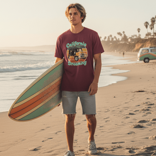 Man holding a surfboard on a beach with a California Dreaming Mini Moke Tee 
