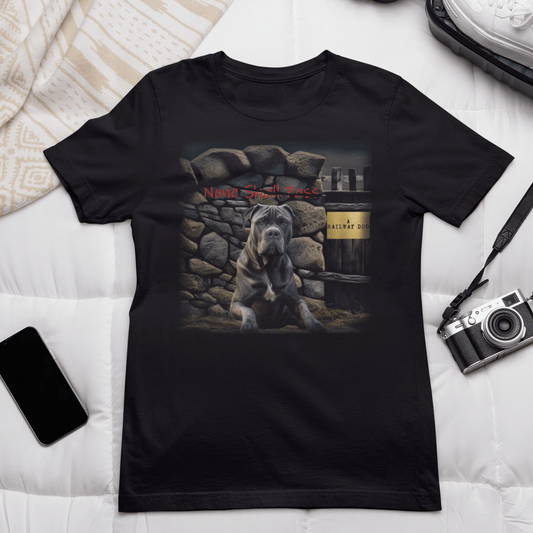 Flat-lay bed mockup of a black graphic t-shirt surrounded by a vintage camera, sneakers, and smartphone, featuring an imposing Cane Corso Mastiff seated before a rugged stone wall with red graffiti text reading "None Shall Pass" and "A Railway Dog" wooden plaque text.