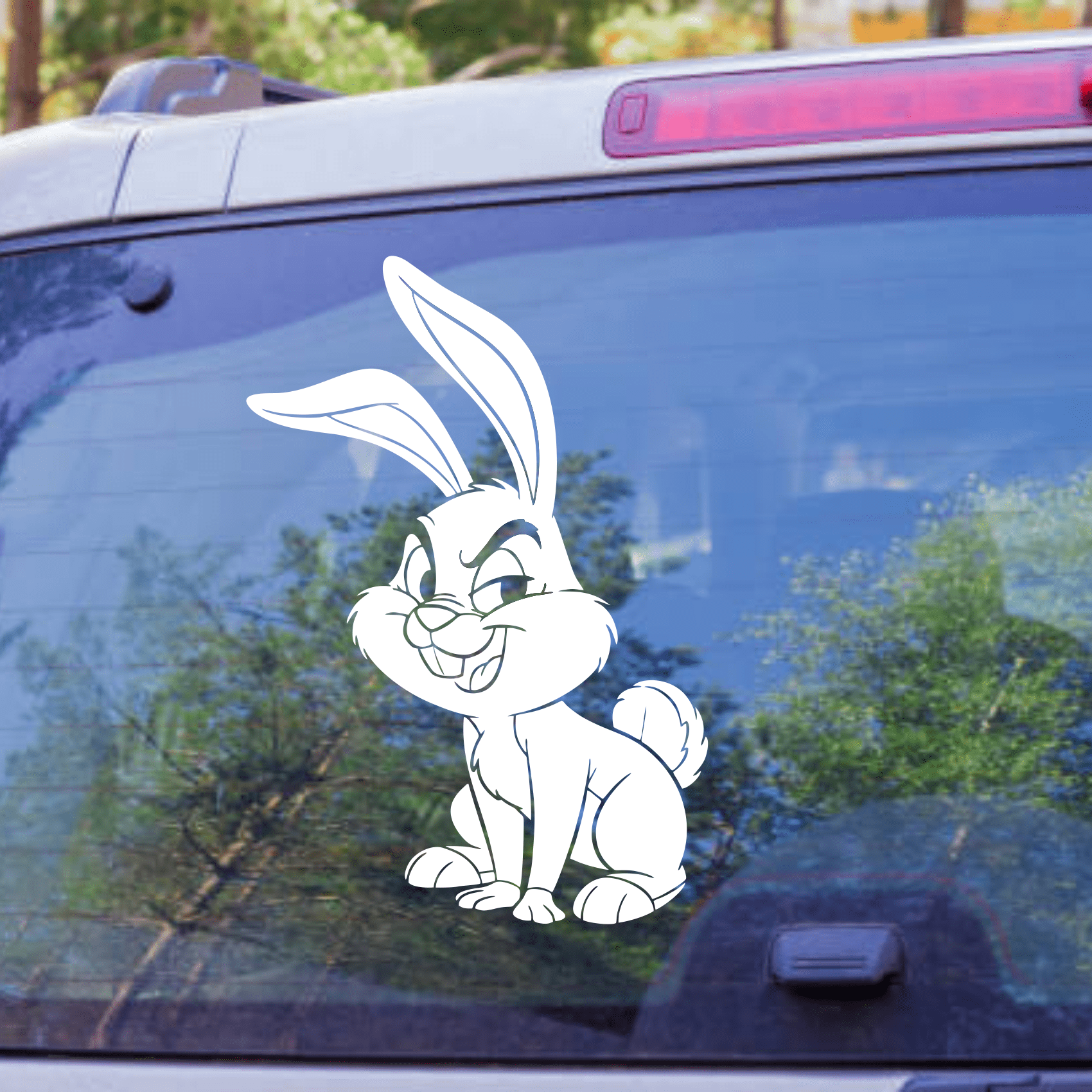 Cartoon rabbit decal on a car window with trees in the background