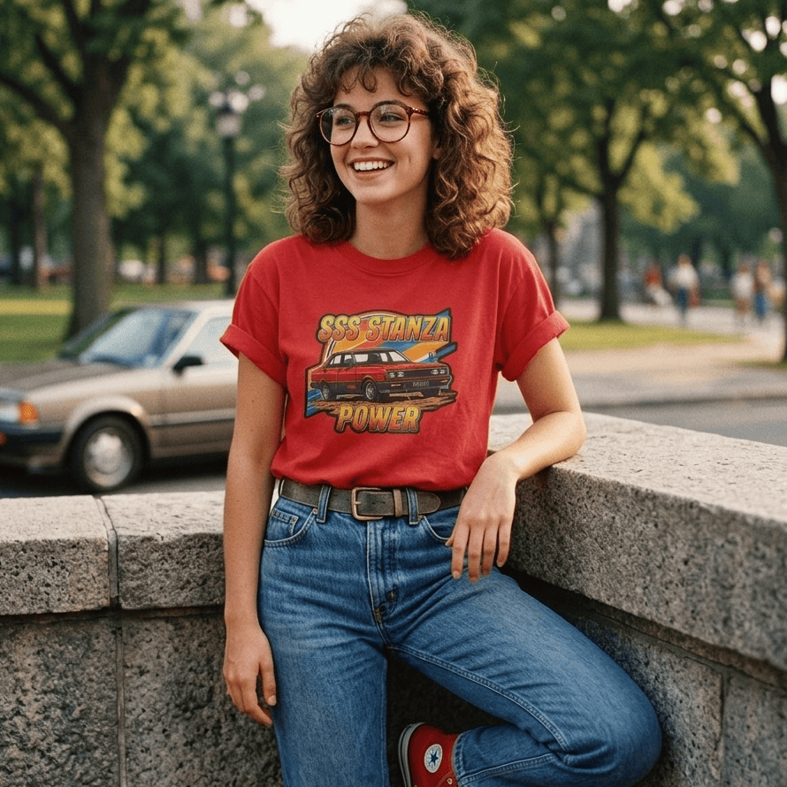 Person wearing a red Datsun Stanza SSS t-shirt with graphic design, sitting on a stone wall outdoors.