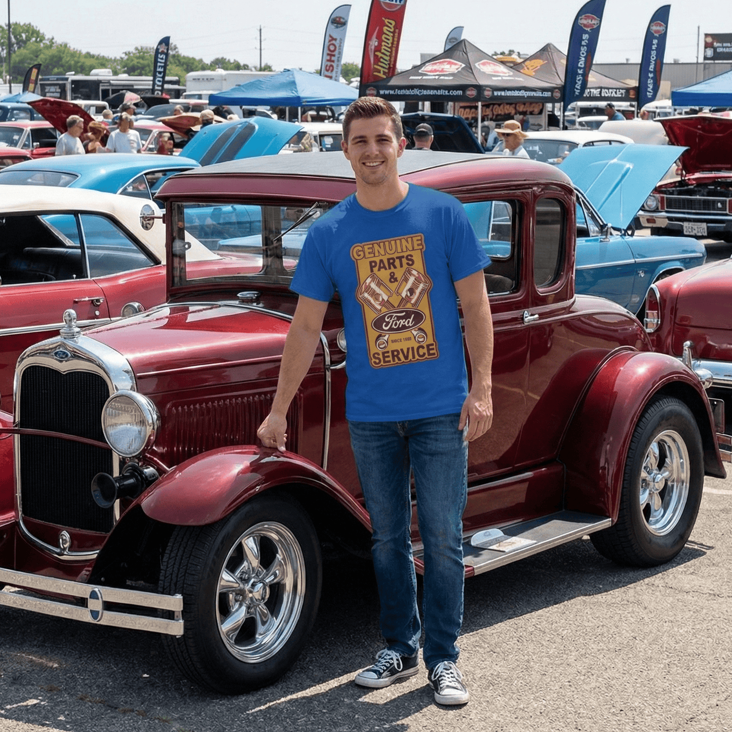 Man standing next to a classic red car at a car show with other vintage cars and attendees in the background.