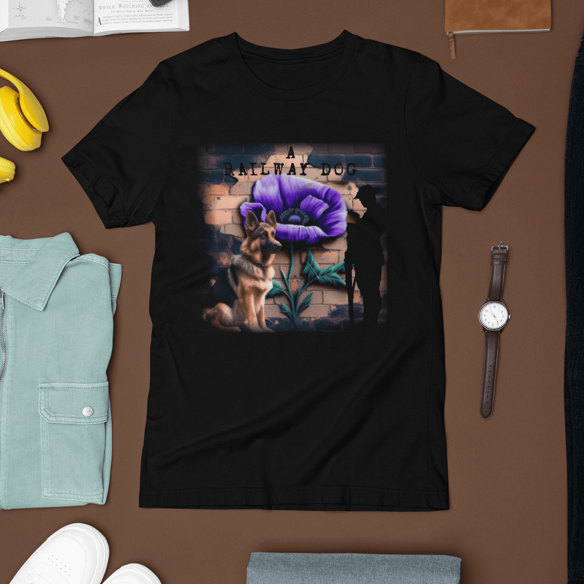 Flat-lay travel outfit mockup featuring a black graphic t-shirt surrounded by a watch, light jacket, and headphones, printed with a German Shepherd sitting beside a large purple poppy mural and soldier silhouette against a brick wall with "A Railway Dog" text.