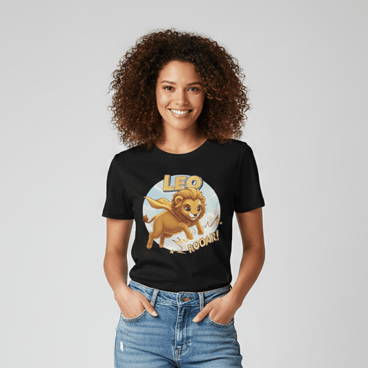 A smiling young woman with curly brown hair wearing a black graphic t-shirt featuring a cartoon lion superhero and the text "LEO ROAR!". She is paired with light-wash distressed denim jeans and white sneakers, standing against a neutral grey studio background.