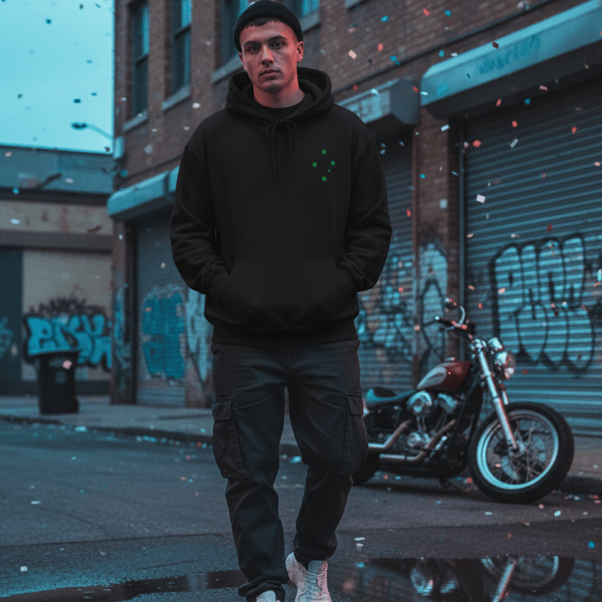 Male model wearing a black, oversized hoodie with a distressed Australian Flag graphic on the back, posed casually in an urban streetwear setting