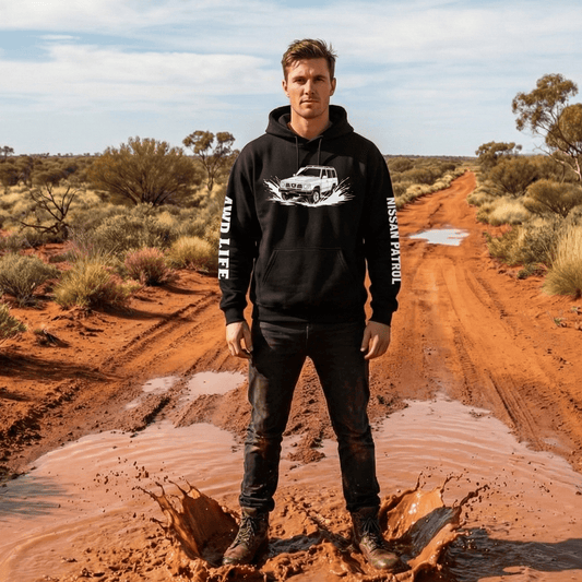 Black pullover hoodie featuring a white line-art illustration of a vintage Nissan Patrol 4x4 splashing through water. The hoodie features white text running down the length of both sleeves.