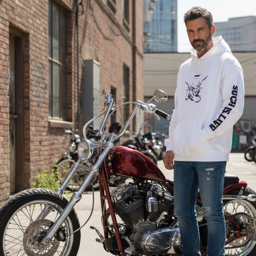 Man in a white hoodie standing next to a red motorcycle in an urban setting