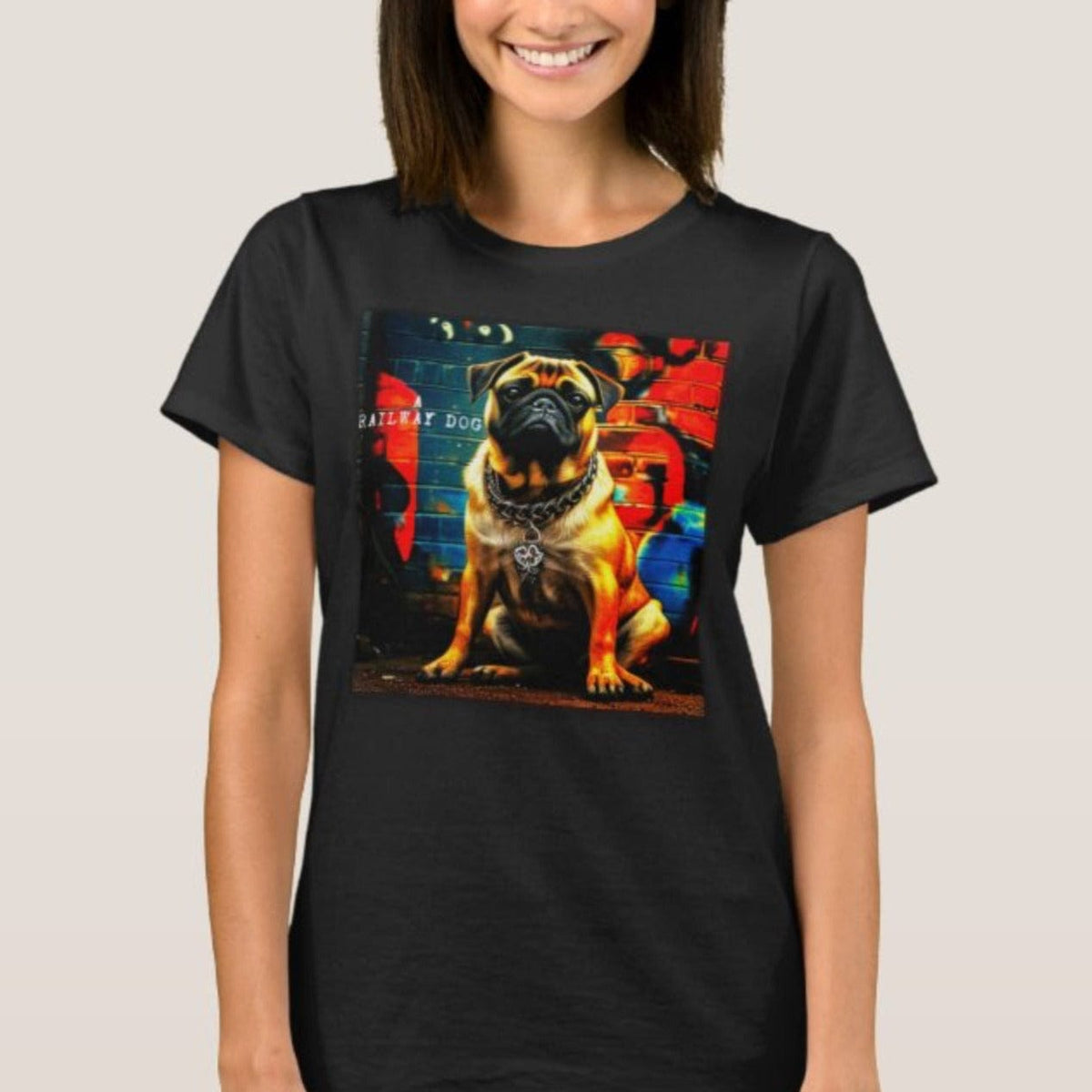 Smiling woman wearing a black graphic t-shirt featuring a fawn Pug with a heavy chain collar sitting in front of a colorful graffiti brick wall mural with "A Railway Dog" stencil text.