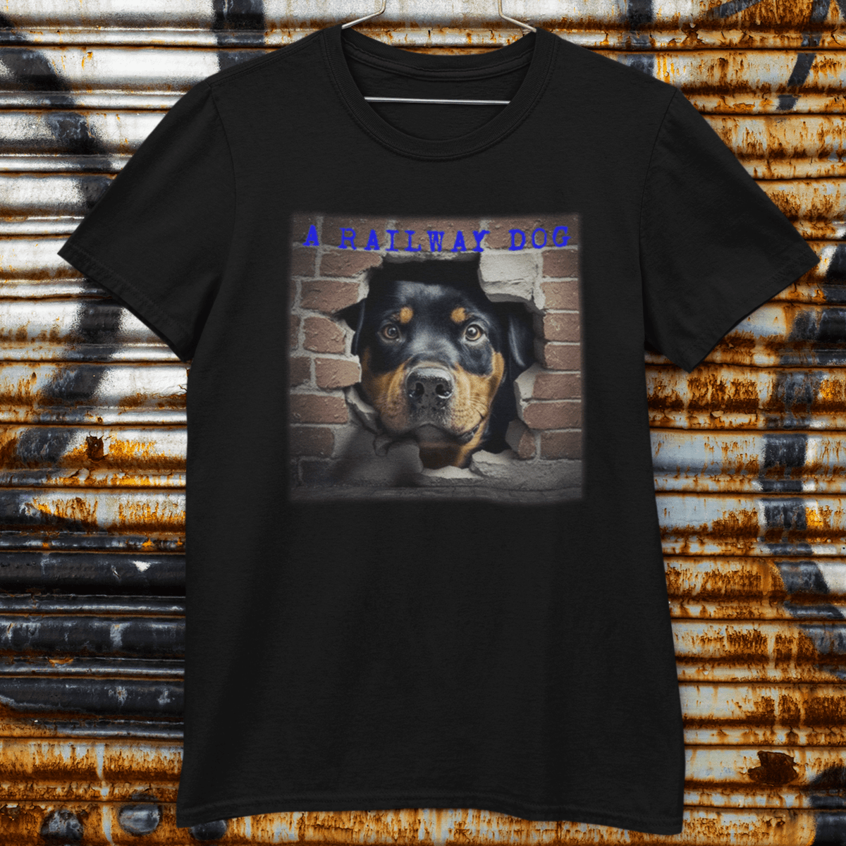 Black graphic t-shirt displayed on a wire hanger against a weathered, rusty roller shutter, featuring an urban art design of a Rottweiler peering through a broken brick wall opening beneath blue "A Railway Dog" text.