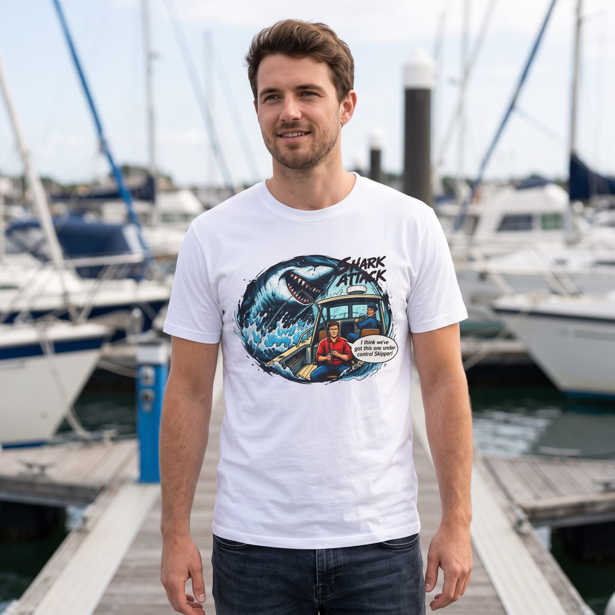 Man wearing white Shark Attack comic graphic t-shirt standing on marina dock with boats in background