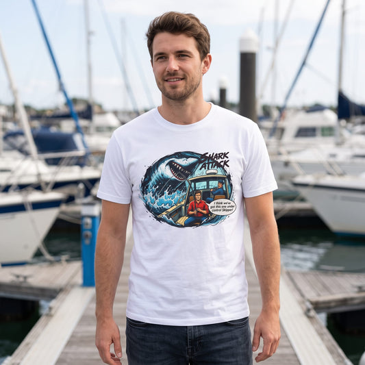Man wearing white Shark Attack comic graphic t-shirt standing on marina dock with boats in background