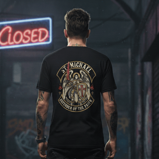 A man stands with his back to the camera in a dark, atmospheric alleyway at night. He is wearing a black t-shirt featuring a large graphic of St. Michael the Archangel in gold and red tones, accompanied by the text "Defender of the Faith."
He is dressed in dark slim-fit jeans and rugged black boots. The alley is dimly lit with mist on the ground, graffiti on the brick walls, and a glowing blue and red "CLOSED" neon sign hanging in the background.