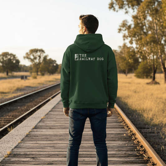 Person wearing a green hoodie with 'The Railway Dog' logo standing on wooden train tracks in a natural setting.