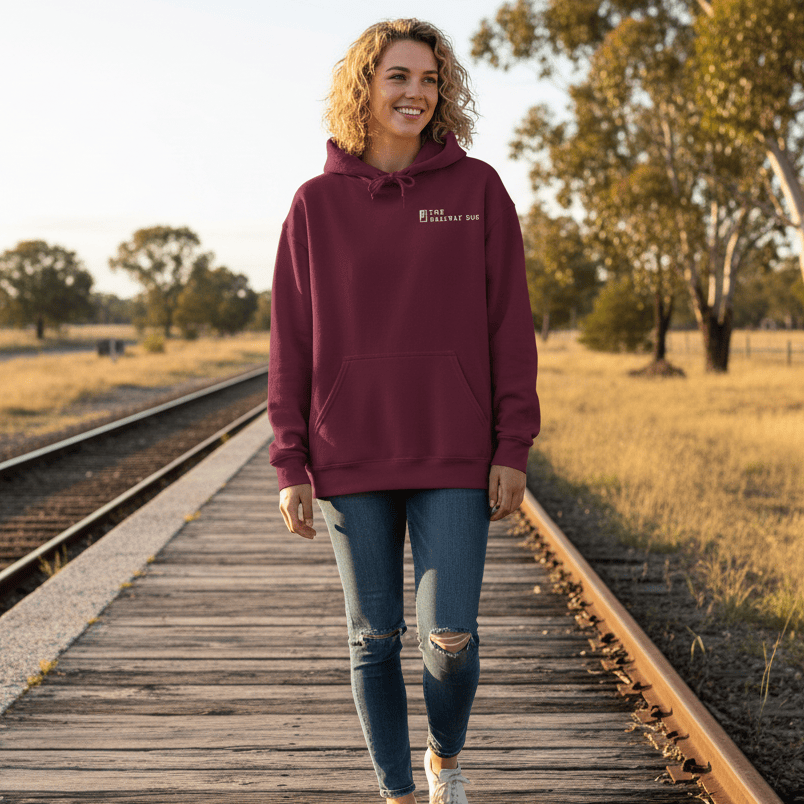 Woman wearing a maroon hoodie with a The Railway Dog logo on a wooden platform by train tracks.