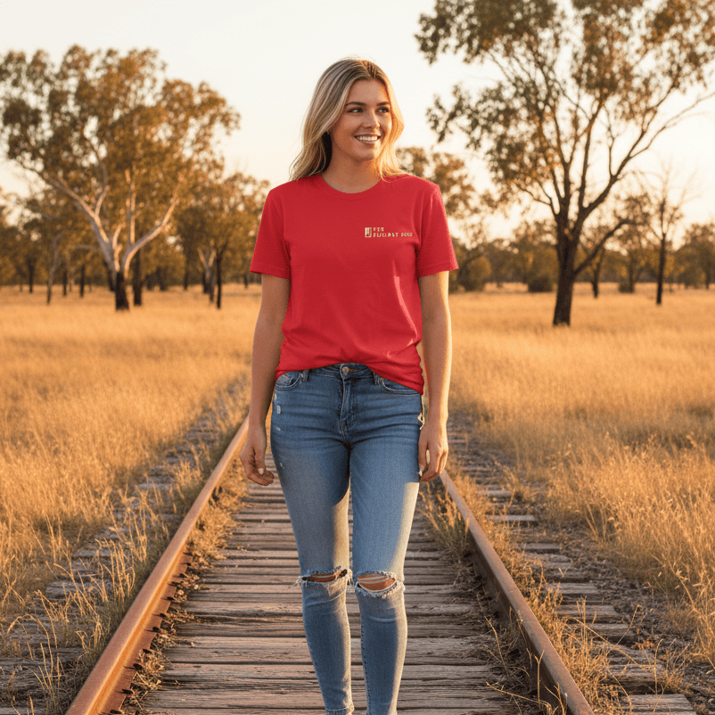 Woman in a red The Railway Dog t-shirt and jeans standing on a railway track in a field at sunset.
