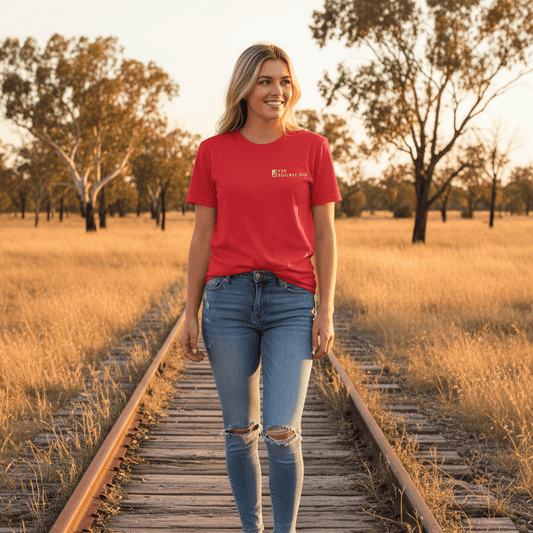 Woman in a red The Railway Dog t-shirt and jeans standing on a railway track in a field at sunset.