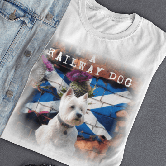 Flat-lay mockup featuring a white graphic t-shirt styled next to a light denim jacket, showcasing a West Highland White Terrier in front of a brick wall mural of the Scottish Saltire flag and purple thistles with "A Railway Dog" stencil text.