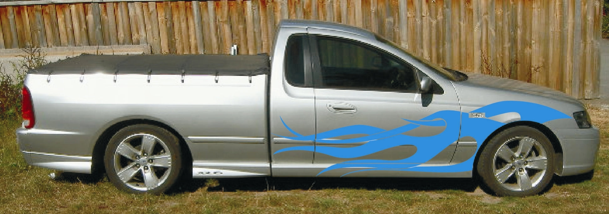 Silver pickup truck with blue graphics parked on grass next to a wooden fence