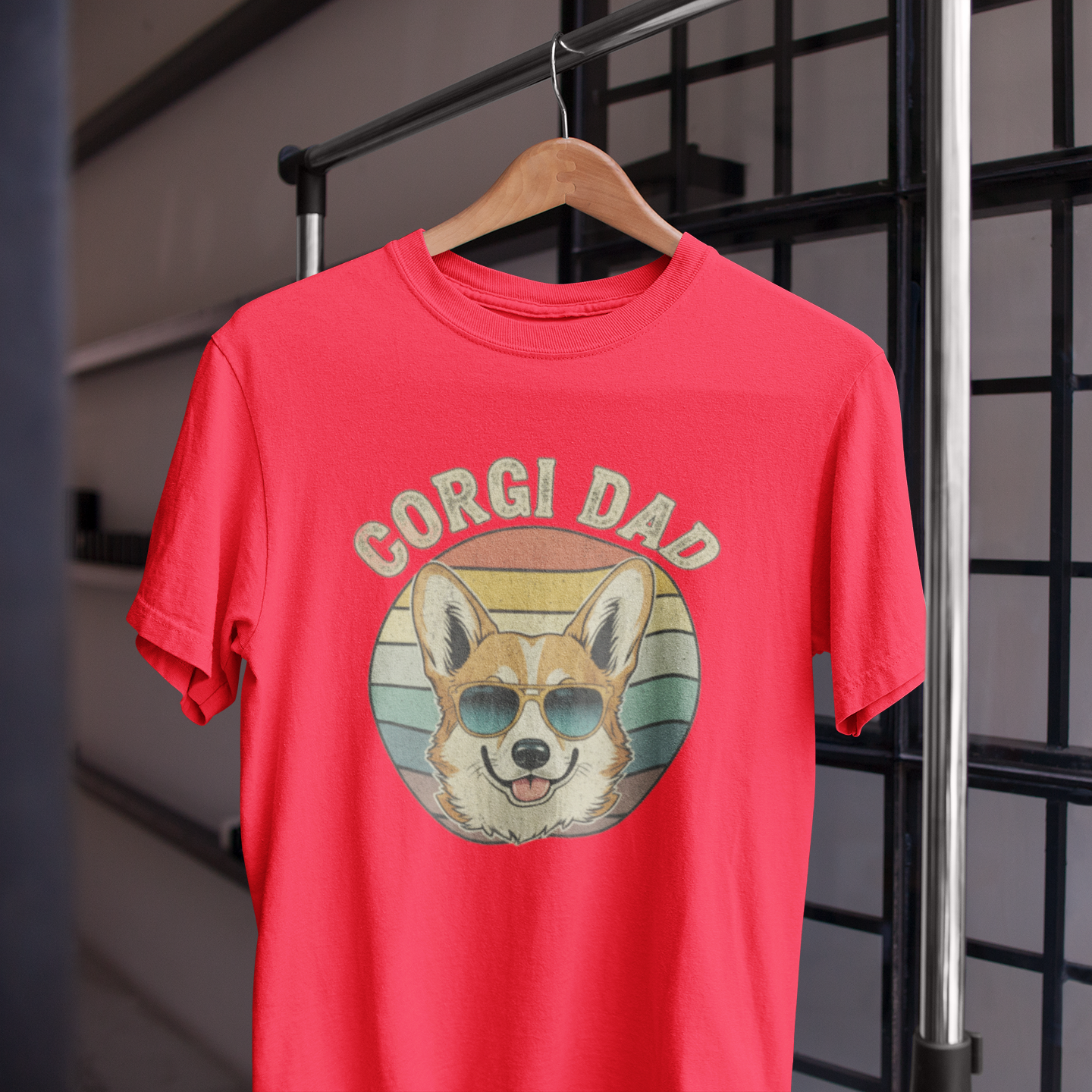 Red t-shirt with 'Corgi Dad' graphic on a hanger against a metal grid background