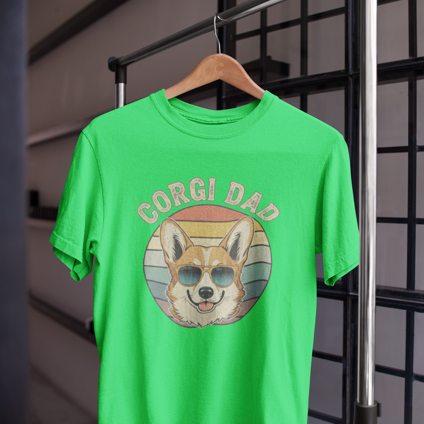 Green t-shirt with 'Corgi Dad' graphic on a hanger against a black metal grid background