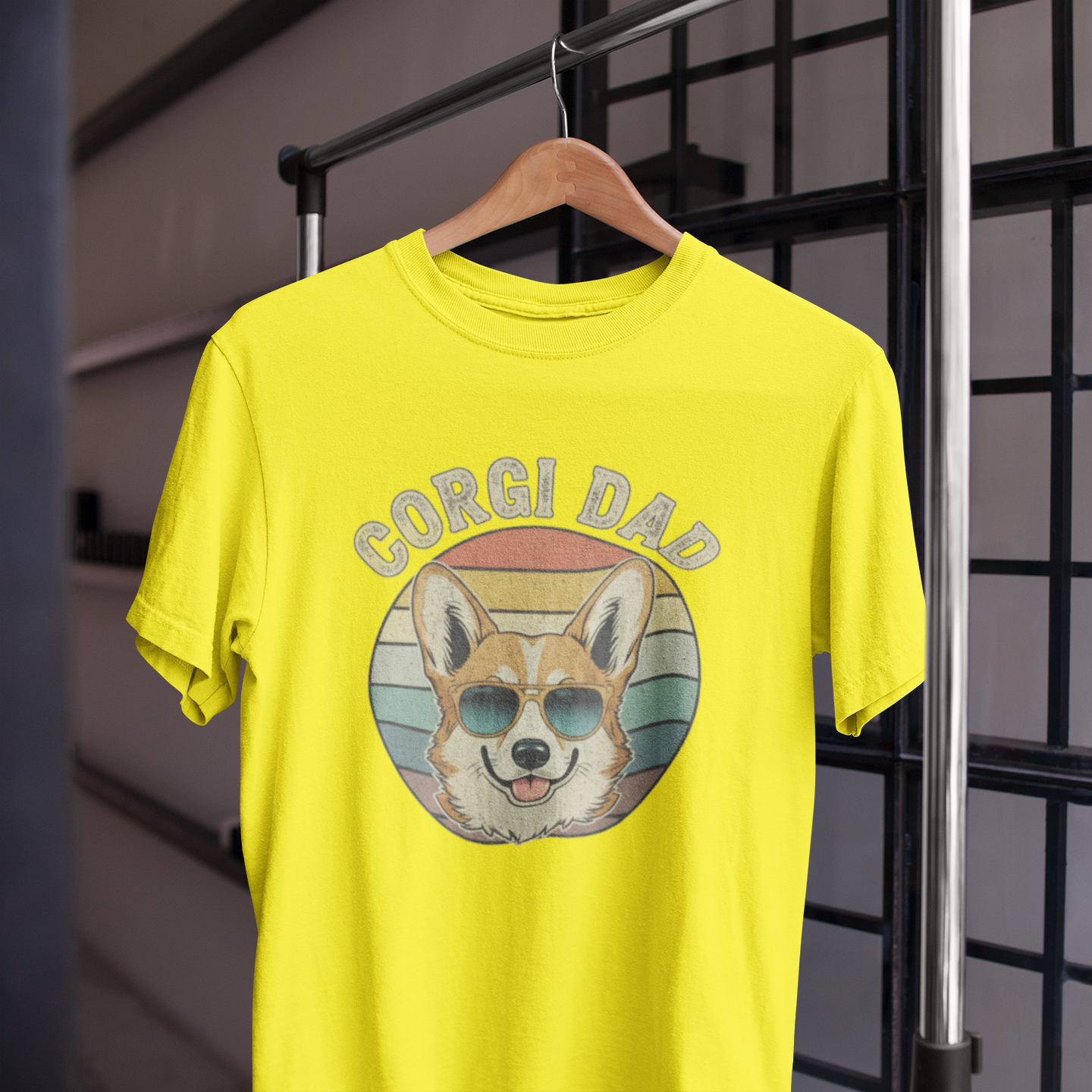 Yellow t-shirt with 'Corgi Dad' graphic on a hanger against a grid background