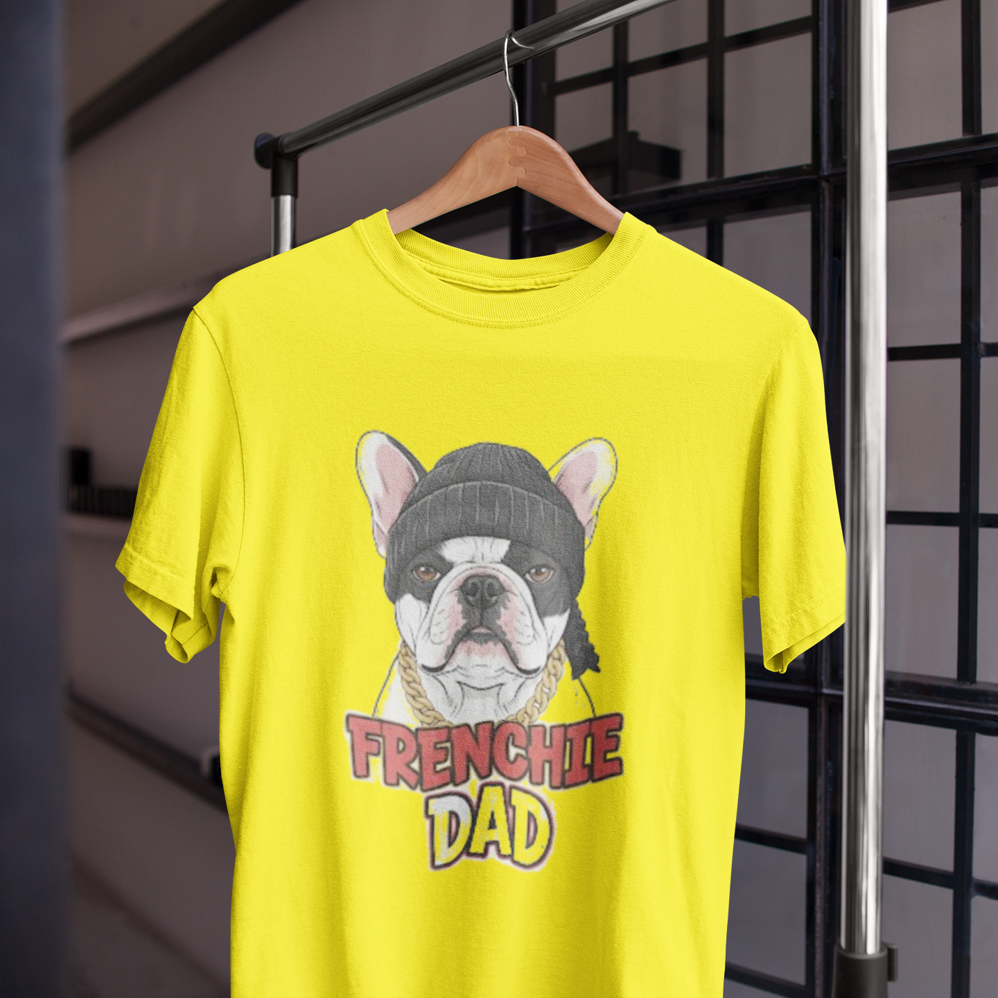 Yellow t-shirt with a dog graphic and 'FRENCHIE DAD' text on a hanger against a grid background