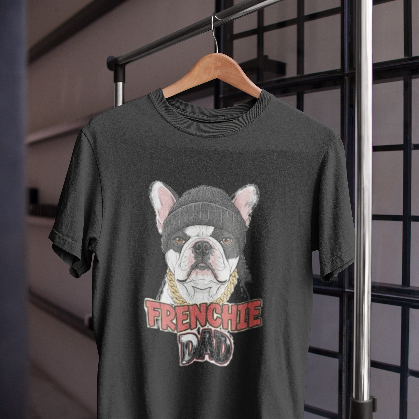 Black t-shirt with a graphic of a bulldog wearing a beanie and 'FRENCHIE DAD' text, hanging on a wooden hanger.