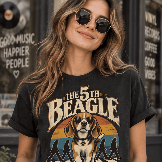 A woman wearing the 5th Beagle retro graphic t-shirt in washed black, posing outside a vintage record shop. The t-shirt features a playful beagle dog with sunglasses on a zebra crossing, with the text "The 5th Beagle - With a Little Help from My Furry Friends."